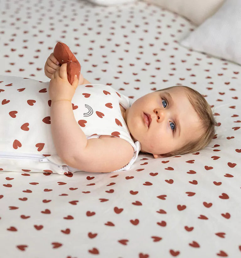 Un bébé allongé sur un lit vêtit d'une gigoteuse || Babykare.fr